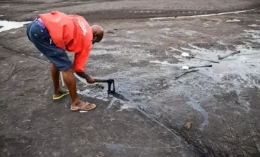 a tour guide in the pitch lake in la brea, trinidad lifts the roar pitch with a piece of wood.-2