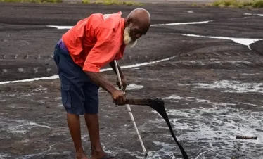 a tour guide in the pitch lake in la brea, trinidad lifts the roar pitch with a piece of wood.