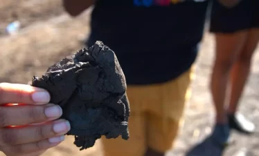 a visitor holding a piece of raw pitch at the la brea pitch lake southern trinidad, the largest natural deposit of asphalt in the world. Known to many as the 8th wonder