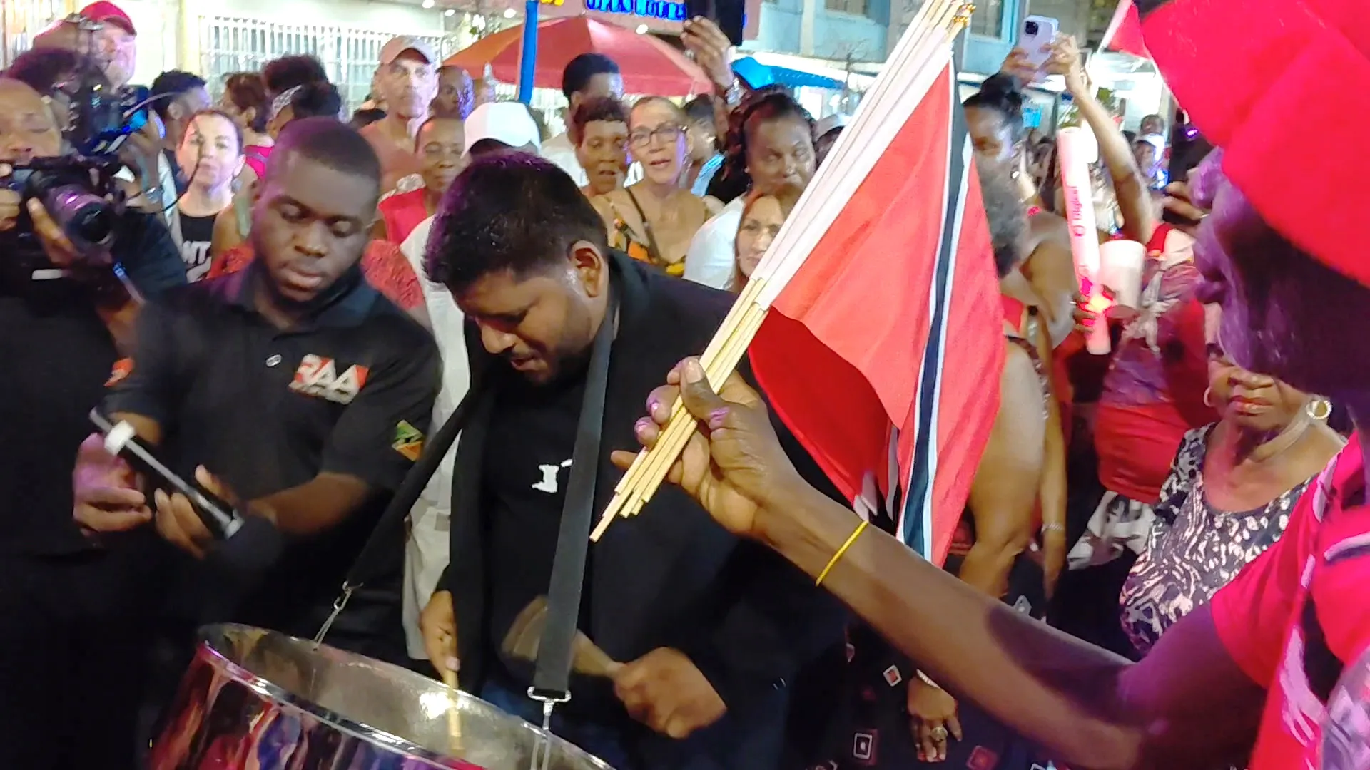Pan man playing the steelpan strapped around his neck in the midst of a large crowd